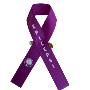 Lila band i tyg med epilepsimärke i blått och vitt och texten epilepsi i vit text. Säkerhetsnål i gul metall.