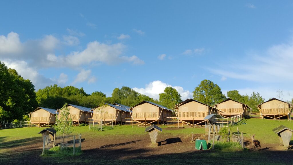 Glampingtältstugor mot bakgrund av grön hage och blå himmel,